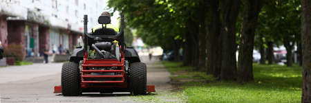 Close-up of professional lawn mower with worker after cutting grass in city park. Gardener using auto lawn mower in urban square. Person using special equipmentsの写真素材