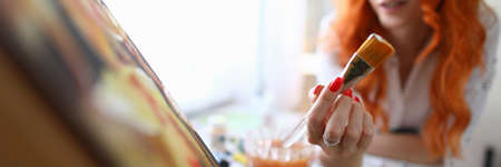 Close-up of woman holding natural paintbrush. Beautiful red haired artist painting on canvas at home. Creative process. Idea for masterpiece. Art and spare time for hobby conceptの写真素材