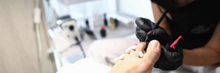 Close-up of pedicurist doing bright pedicure. Worker covering toe nails with pink nail polish. Client on treatments in beauty saloon. Beauty salon and chiropody conceptの写真素材