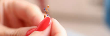 Close-up of dressmaker carefully thread a needle. Creative work. Female with beautiful red manicure....