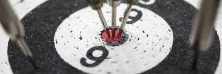 Close-up of dart board. Darts hitting in reaching central target. Excitement. Black and white chipboard with javelins. Goal achievement and fortune conceptの写真素材