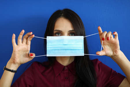 Beautiful woman holding in hands blue protective mask putting it on closeup