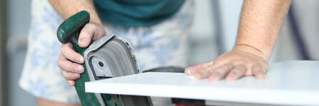 Close-up of carpenter working with electrical equipment for polishing wooden surface. Professional...