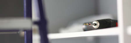 Close-up of electrical drill instrument laying on white shelf. Special metal nozzle for tool. Ladder...