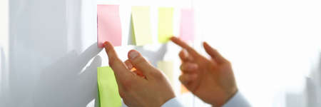 Close-up of worker hand holding colorful papers for notes with information. Person preparing for...