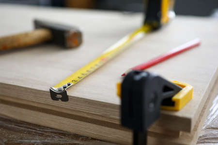 Close-up of carpenter tools and instruments for joinery work. Wooden plank fixing in vise, measuring tape, hammer and pencil. Carpentry workshop conceptの写真素材