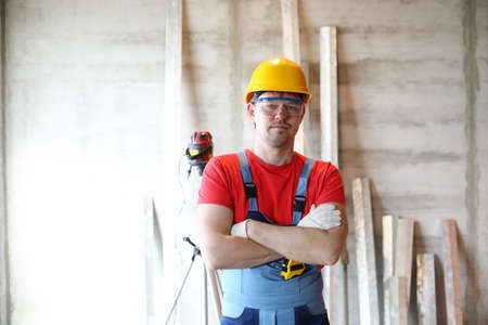 Portrait of professional worker posing with crossed arms in protective uniform and yellow helmet....