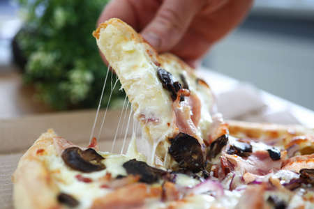 Male arms taking big piece of crusty fresh pizza at working table close-up