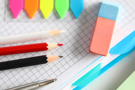 Top view of red and black pencils. Silver pen and eraser. Colourful bookmarks on desktop. Empty notebook sheet. Paper for notes and creative ideas. Office stationery conceptの写真素材