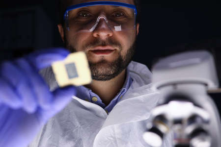 Portrait of concentrated professional technician in uniform at work. Man in eye-glasses looking...