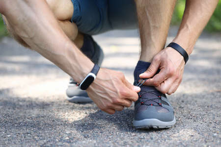 Close-up of sporty male person hands tying up shoelace. Stylish grey sneakers for running. Man ready...