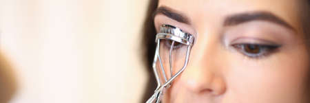 Close-up of female master curling eyelashes with special metal equipment. Beautiful client with lovely natural makeup. Beauty salon and care treatment conceptの写真素材