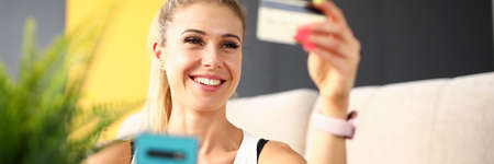 Beautiful blonde woman looks at a credit card and laughs. Concept of using online banking on a...