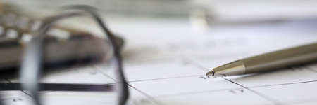 Close-up of calendar and black glasses laying on working table. Pen for writing. Busy day. Career growth and development. Calculator on desk. Business and planning conceptの写真素材