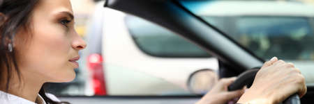 Young beautiful woman in a shirt sits at the wheel of a car. The driver is stuck in a traffic jam
