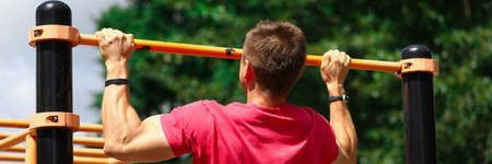 Portrait of strong sportsman doing strength exercises. Athlete pulling up on horizontal bar on athletic field. Training and lifestyle. Sport and body-building conceptの写真素材