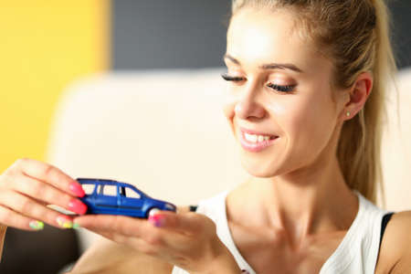 Portrait of smiling pretty female with natural makeup. Woman holding small car figure on hand....