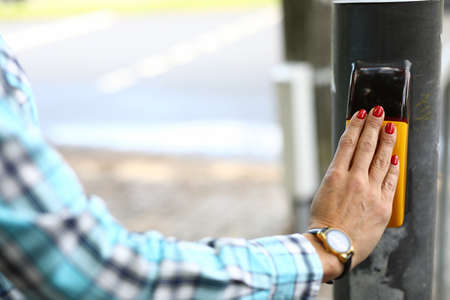 Close-up of woman pressing knob on metal pole. Inscription on smart screen please wait. Female with...