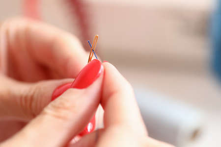 Close-up of dressmaker carefully thread a needle. Creative work. Female with beautiful red manicure....