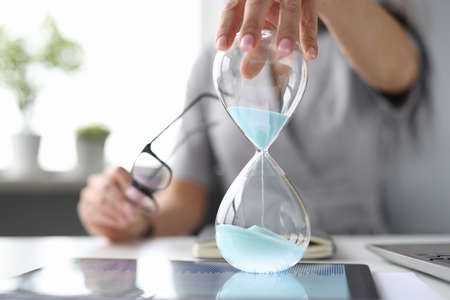 Female hand on desktop holds an hourglass. Time management in business concept
