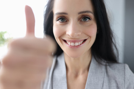 Smiling brunette businesswoman showing thumb up in office. Successful business development concept