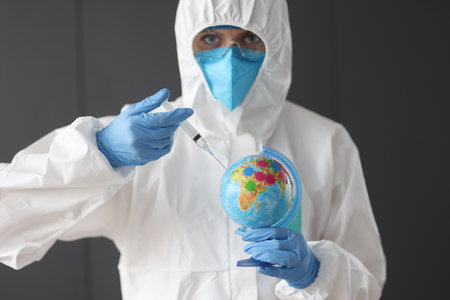 Doctor in anti-plague suit making injection into globe. Vaccination against covid19 conceptの写真素材
