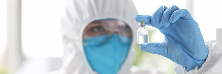 Researcher in protective suit looks at medicine bottle. Development of new drugs concept