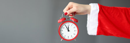 Hand in santa claus costume holds red alarm clock. New Year and Christmas celebration concept
