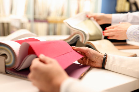 Womens hands choosing color of fabric in curtain catalog in workshop closeup. Colors in interior...