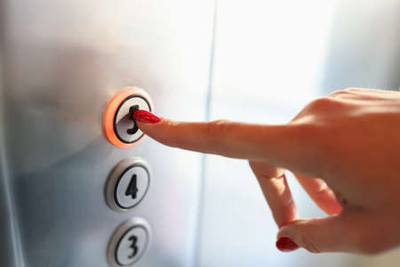 Womans hand pressing button of elevator to fifth floor close-up. Repair and maintenance of elevators...