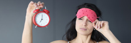 Woman takes off her sleep mask and looks at alarm clock. Sleep problems concept
