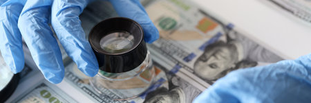 Checking American banknotes with magnifying glass. Counterfeiting banknotes conceptの写真素材