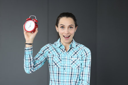 Surprised woman holds red alarm clock in her hand. Time management in business conceptの写真素材
