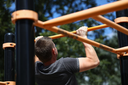 Portrait of man working out on sports ground. Sportsman pulling up on horizontal bar on athletic...