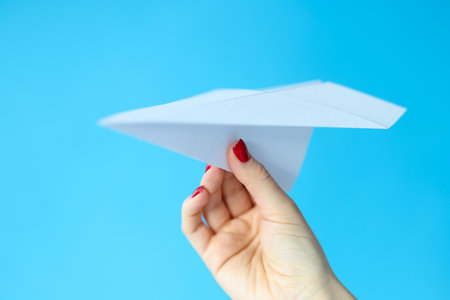 Female hand holding paper plane on blue background. Air transportation conceptの写真素材