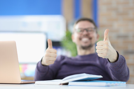 Smiling man showing thumbs up in office closeup. Remote work freelance conceptの写真素材