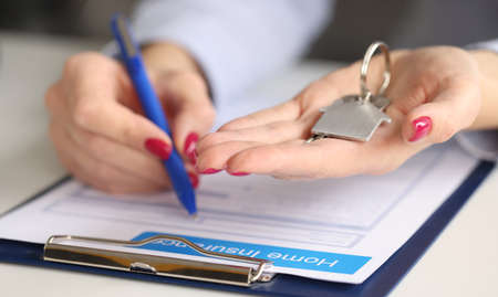 Female hands hold house keys and fill out real estate insurance. Property insurance concept