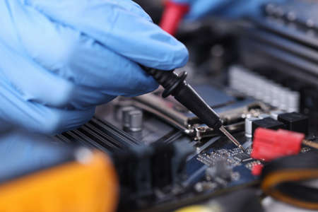 Gloved technician with tester checks motherboard. Computer repair conceptの写真素材