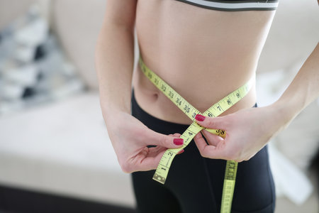Woman measuring her waist with centimeter tape at home. Fast weight loss conceptの写真素材