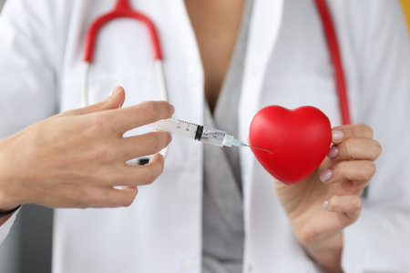 Doctor injecting medicine into red toy heart closeup. Treatment of diseases of cardiovascular system conceptの写真素材