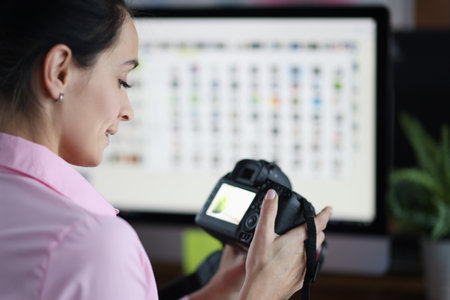 Young woman holding camera in hands and looking at photos. Freelance profession photographer conceptの写真素材