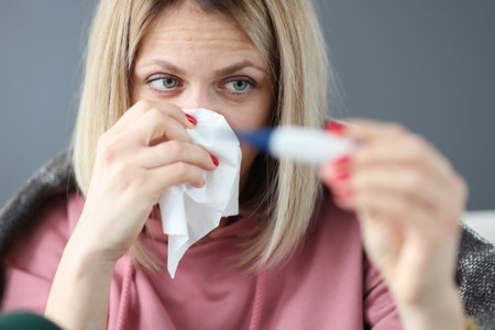 Sick woman holding infrared thermometer and paper napkin. Ambulatory treatment concept