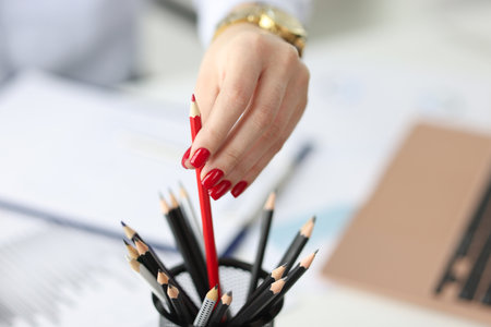 Female hand with red manicure pulling out pencil in office closeup. Main tasks in business conceptの写真素材