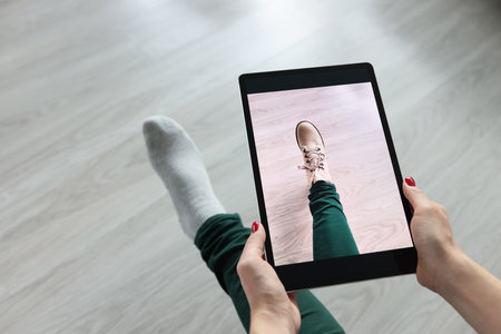 Woman holding tablet over her leg and trying on shoes closeup. Online dressing room conceptの写真素材