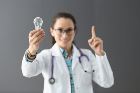 Woman doctor holding light bulb in hands and showing index finger up. New ideas in health care development conceptの写真素材