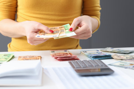 Woman siting at table and holding cash euro bills in her hands closeup. Accounting conceptの写真素材