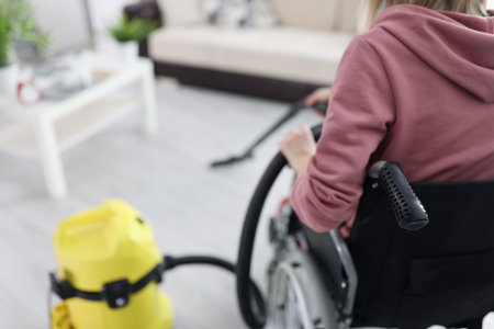 Disabled woman in wheelchair vacuuming floor in apartment. Life of people with disabilities conceptの写真素材