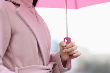 Female hand holding pink umbrella in rain closeup. Weather forecast concept