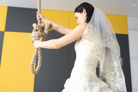 Bride in wedding dress holding rope for suicide. Psychological help in family conflicts conceptの写真素材