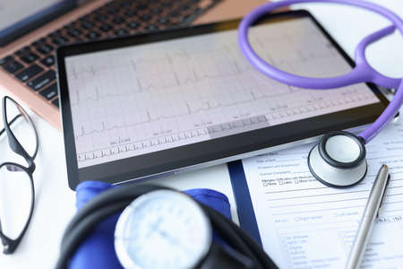 Digital tablet with electrocardiogram lying on doctors desk closeup. Ecg diagnosis of rhythm disturbances conceptの写真素材